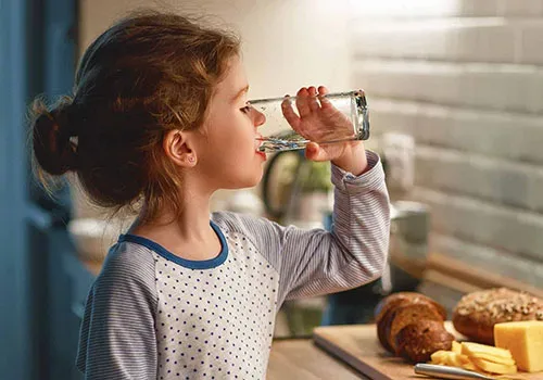 Niña bebe agua pura en la cocina